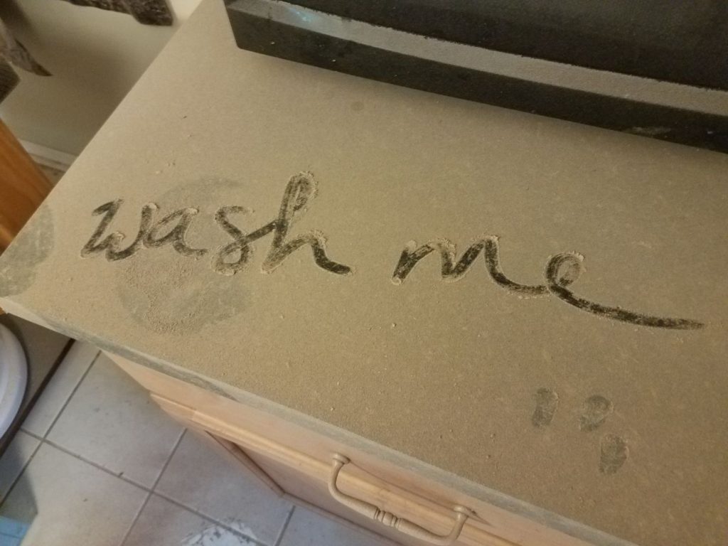 photograph of a counter covered in dust with the words wash me written on it